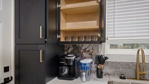 A kitchen with dark cabinets, a coffee maker, a water dispenser, and a sink with a gold faucet.
