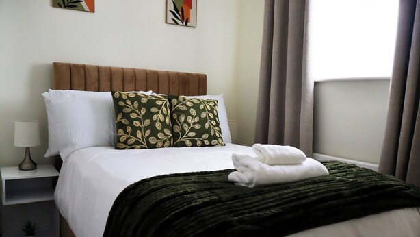 A neatly made bed with white linens, a green patterned pillow, and a dark green blanket. - Cozy, Family Friendly ,Home Away from Home in Aveley, Thurrock (Aveley)