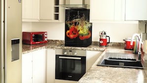 A compact kitchen with a Bosch oven, a red microwave, a coffee maker, and a sink. - Cozy, Family Friendly ,Home Away from Home in Aveley, Thurrock (Aveley)