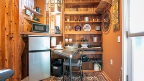 A compact kitchen with a refrigerator, microwave, and coffee maker on the countertop. There is a dining table with chairs and a patterned rug. Shelves above the counter hold various dishes and kitchenware. - Boho Studio on 8th Ave West | Queen Anne, Seattle Near Stadium (Seattle)