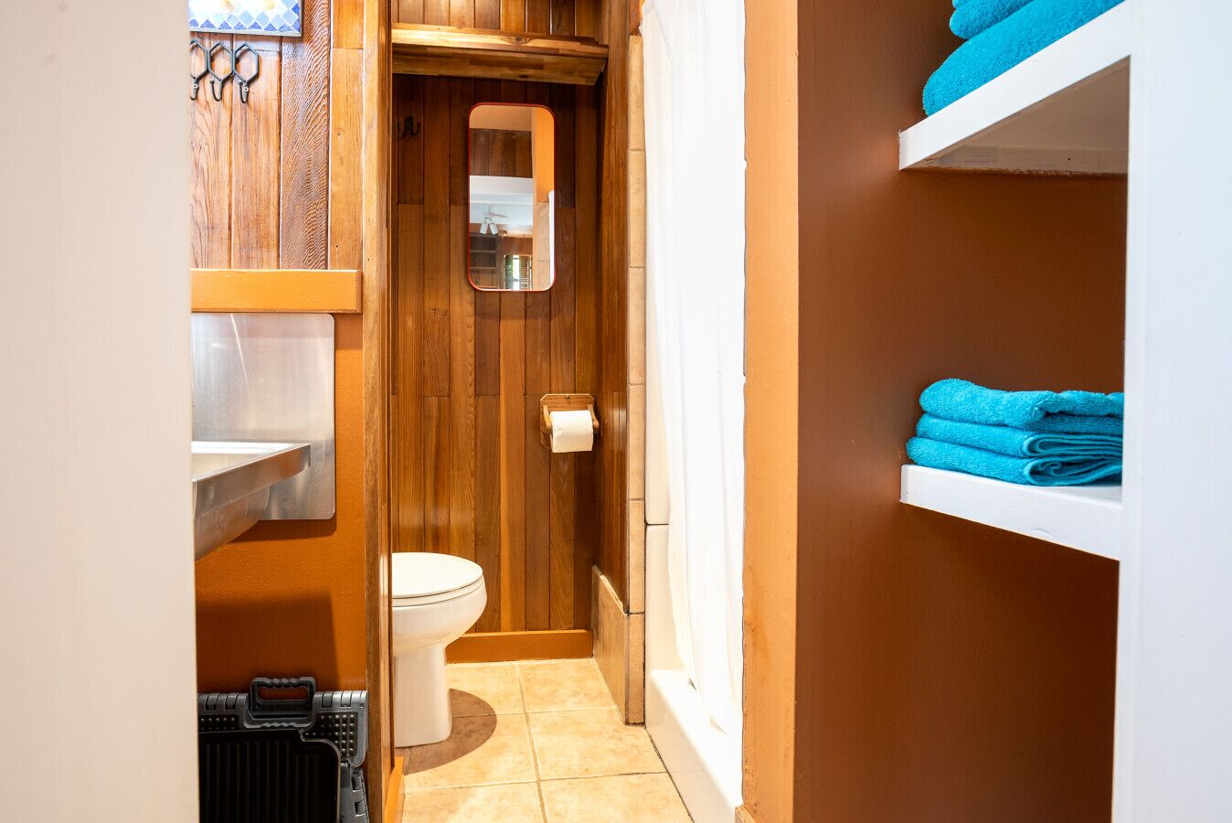 Ein kleines Badezimmer mit Toilette, einem kleinen Spiegel und einem Regal mit gefalteten Handtüchern.