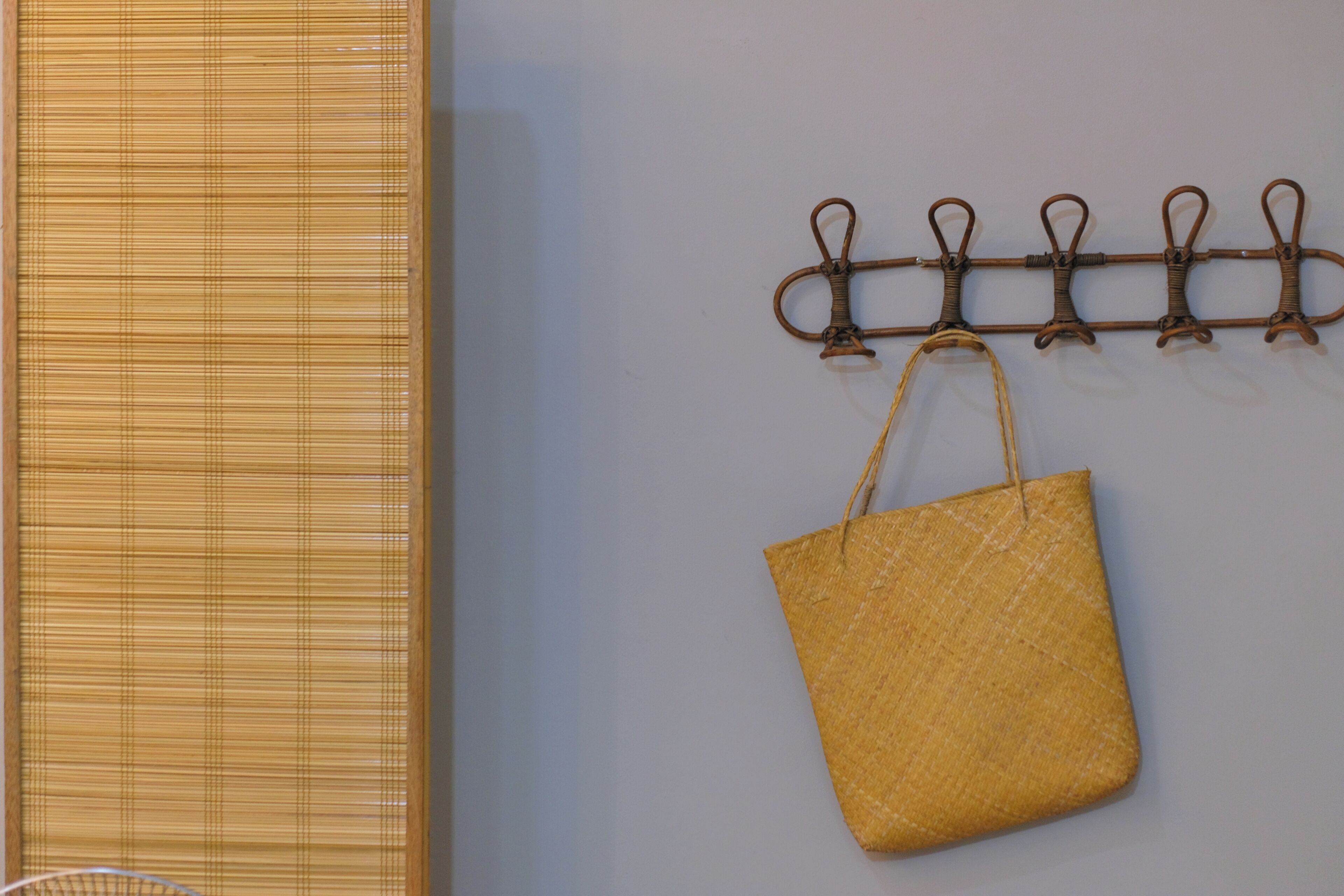 A wall-mounted hook with a woven bag hanging from it.