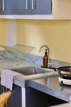 A kitchen with a granite countertop, a stainless steel sink, a dish rack, a soap dispenser, and a frying pan. - 2BR Laid Back Apartment, Near Beach (San Fernando)