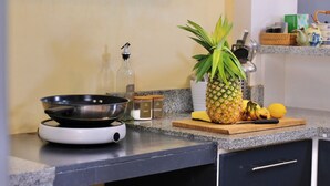 Eine Küchenarbeitsplatte mit einer Bratpfanne, einer Flasche, einer Ananas und einigen Küchenhelfern.
