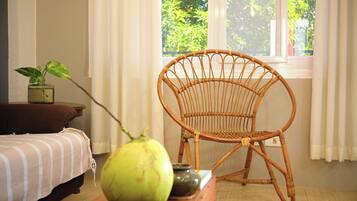 Una silla de mimbre, una cama, una mesa con una fruta verde y una ventana con cortinas.