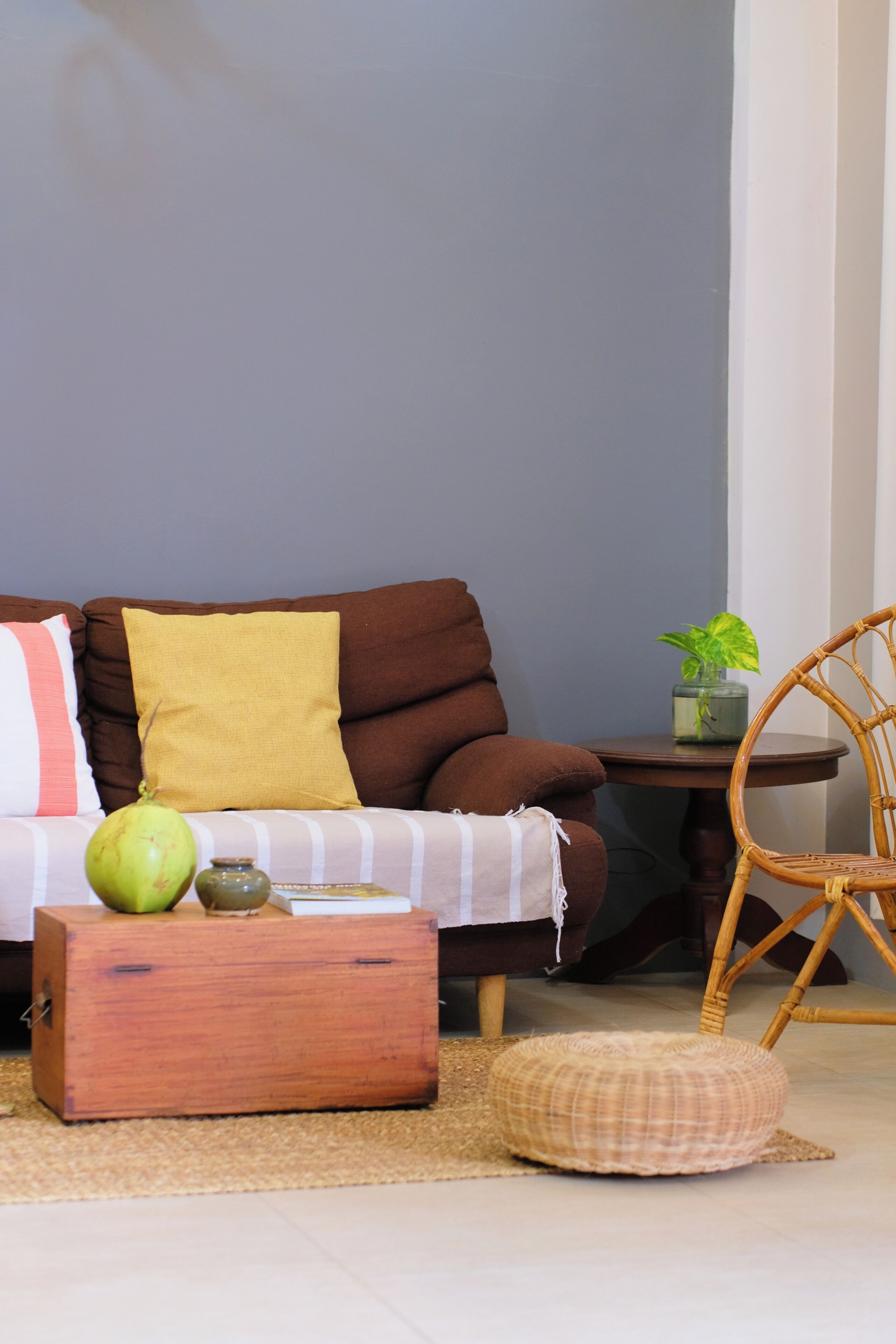A living room with a brown sofa, a wooden coffee table, a wicker chair, and a small potted plant.