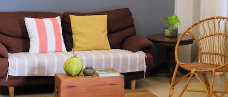 A living room with a brown sofa, a wooden coffee table, a wicker chair, and a small table with a plant.