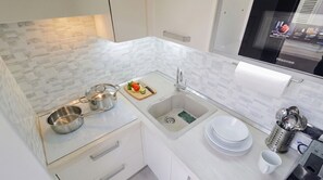 A modern kitchen with white cabinetry, a stainless steel sink, a built-in stove, and a countertop with a cutting board and vegetables. - Vento Mare Apartments & Suites-Palau (Palau)