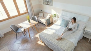 Een slaapkamer met een bed, nachtkastje, stoel, klein tafeltje en een raam.