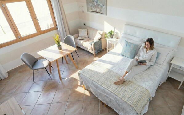A bedroom with a bed, a bedside table, a chair, a small table, and a window. - Vento Mare Apartments & Suites-Palau (Palau)