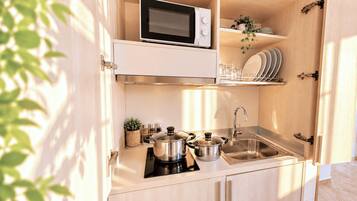 Cocina compacta con microondas, estufa, fregadero y estanterías para vajilla.