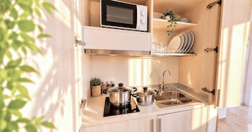 Cocina compacta con microondas, estufa, fregadero y estanterías para vajilla.