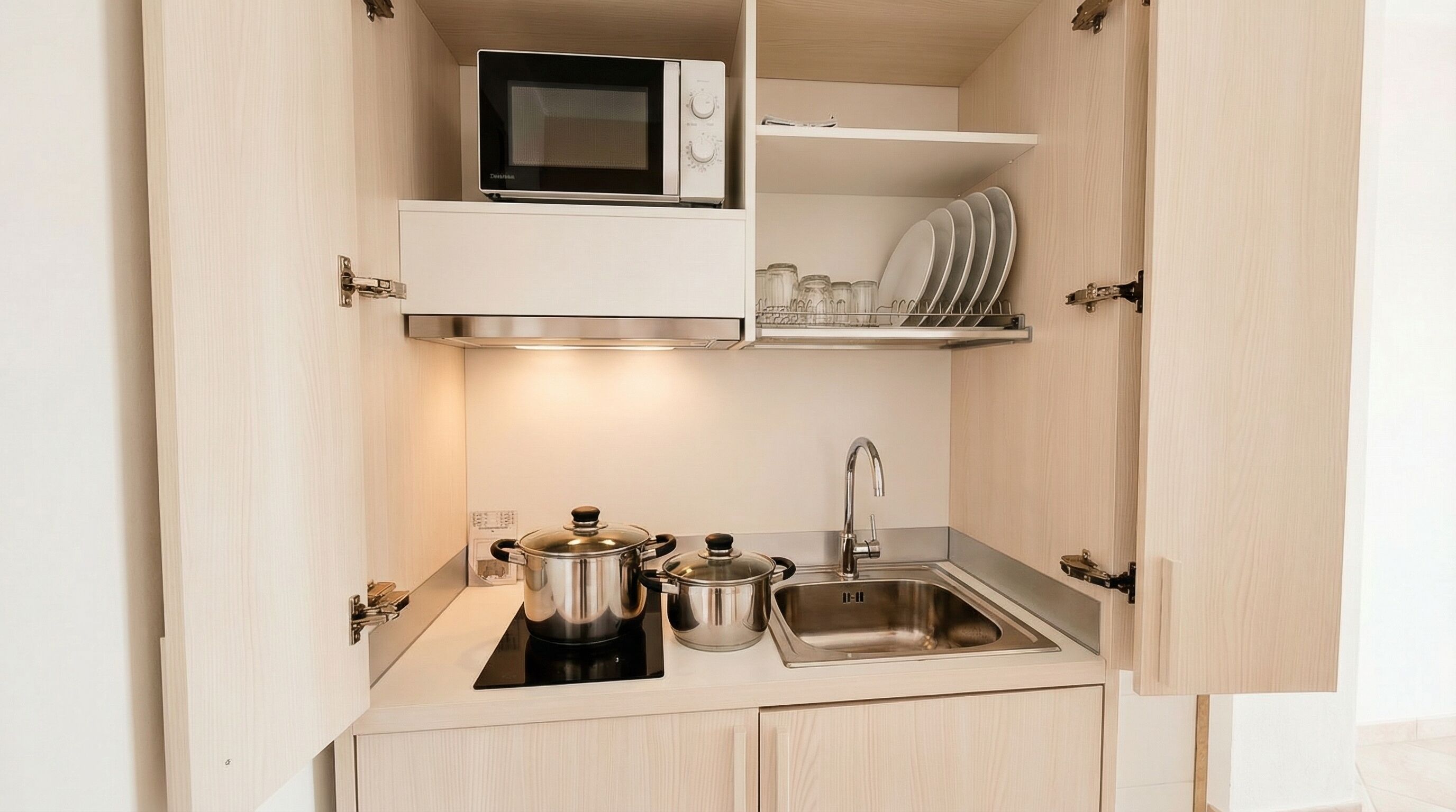 Cocina compacta con microondas, estufa, lavamanos y escurreplatos.