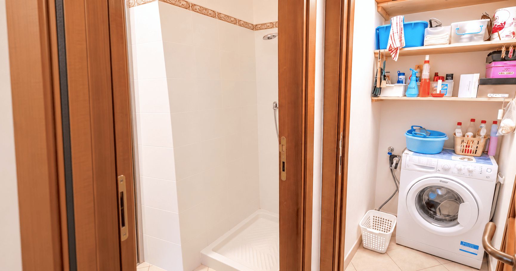 A bathroom with a shower, a washing machine, and shelves with toiletries.