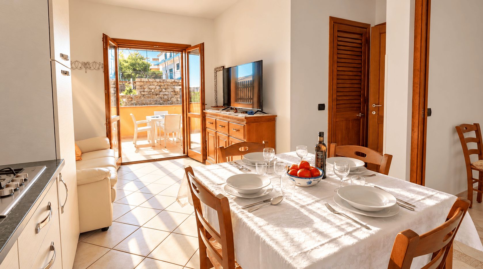 Comedor con una mesa dispuesta para cuatro personas, un televisor y vistas a un balcón con mobiliario exterior.