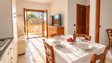 Comedor con una mesa dispuesta para cuatro personas, un televisor y vistas a un balcón con mobiliario exterior.