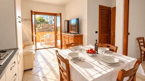A dining area with a table set for four, a television, and a view of a balcony with outdoor furniture. - Vento Mare Apartments & Suites-Palau (Palau)