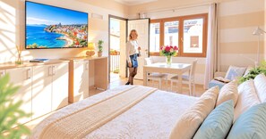 A hotel room with a bed, a TV, a dining table, and a view of the sea. - Vento Mare Apartments & Suites-Palau (Palau)