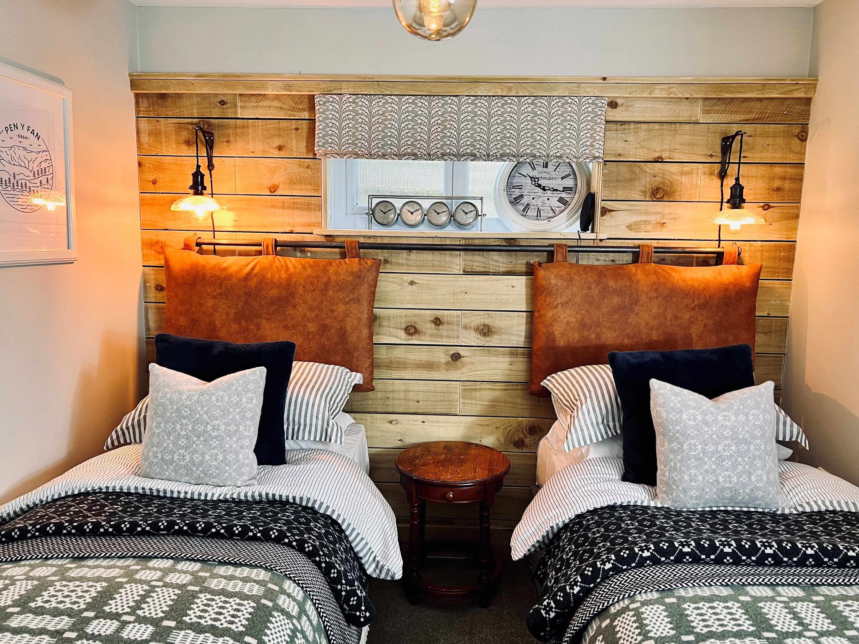 Een gezellige kamer met twee bedden, een klein rond tafeltje en een houten wand met klokken en een kamerkleed.