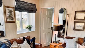 A cozy living room with a brown leather sofa, a matching ottoman, and a wooden coffee table. A large mirror hangs on the wall, and a door leads to another room. - Family Bungalow, Mountain Views, Pets Welcome (Pontsticill)