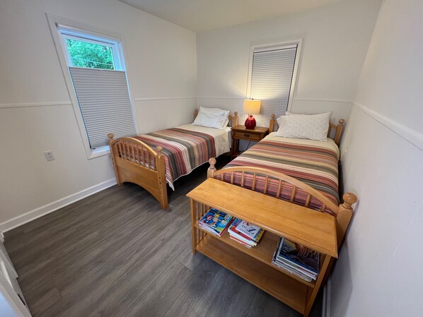 A bedroom with two wooden beds, a nightstand, a lamp, and a bookshelf with books. - Charming 2-bedroom cottage in Buchanan with AC, WiFi, Centrally located! (Buchanan)