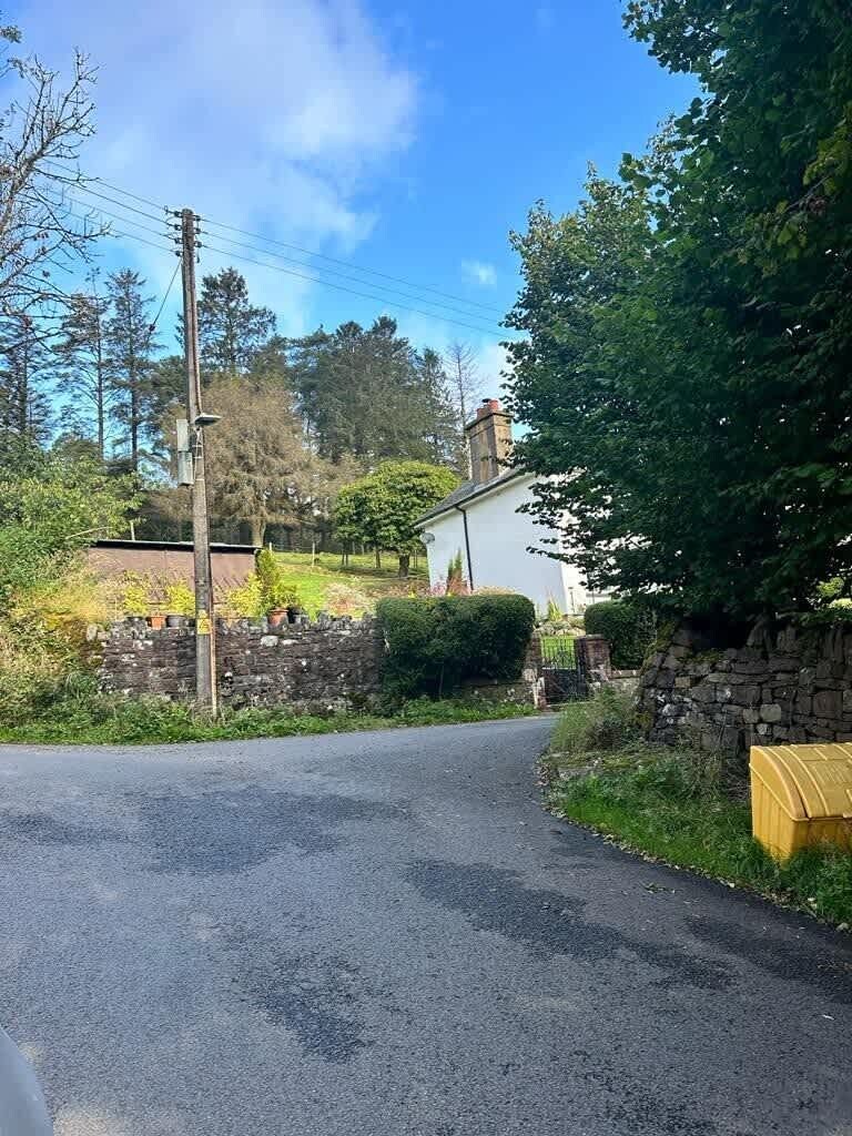 Un chemin de campagne menant à une maison blanche, dotée d’un mur en pierre et d’une boîte aux lettres jaune.