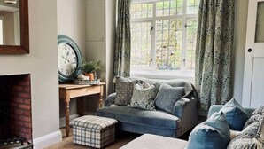 Ein gemütliches Wohnzimmer mit Kamin, einer Couch, einem Couchtisch und einem großen Fenster mit Vorhängen.