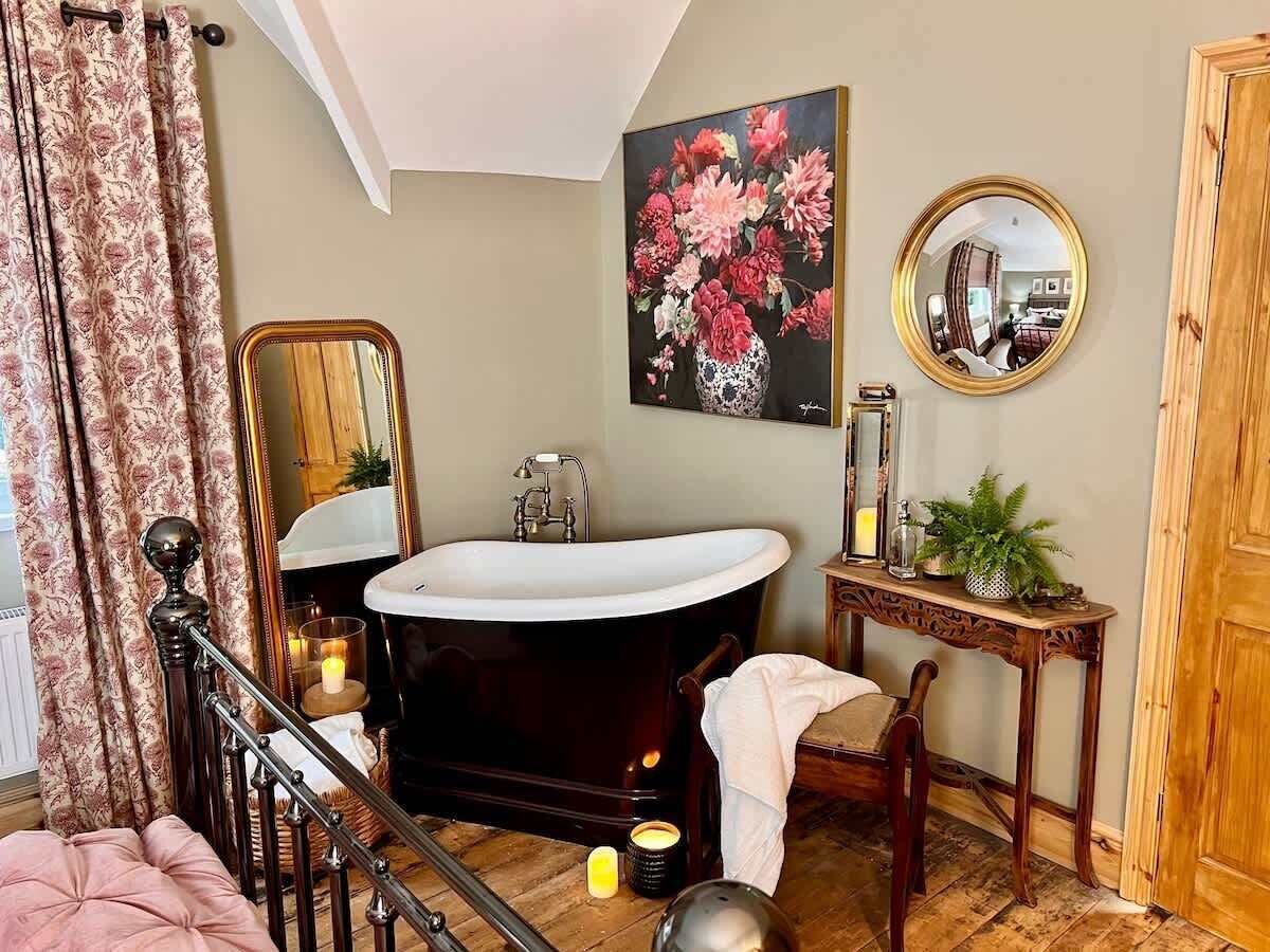 A bathroom with a freestanding bathtub, a wooden vanity, a mirror, and a floral painting on the wall.