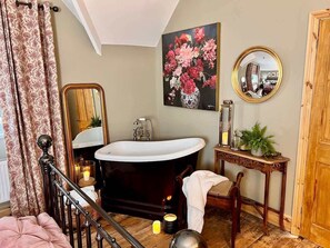 Ein Badezimmer mit einer freistehenden Badewanne, einem Holzwaschtisch, einem Spiegel und einem Blumenbild an der Wand.