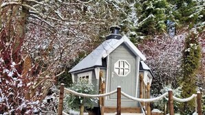 A small, rustic cabin with a steeply pitched roof and a chimney, surrounded by snow-covered trees and a rope barrier. - Charming Cottage w/ Valley Views & BBQ Hut (Pontsticill)