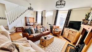 A spacious living room with a sofa, coffee table, and a fireplace. A staircase is visible in the background. - Charming Cottage w/ Valley Views & BBQ Hut (Pontsticill)