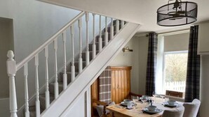 A dining area with a wooden table set for four, a white staircase, and a view of the outdoors through a window. - Charming Cottage w/ Valley Views & BBQ Hut (Pontsticill)
