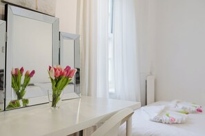 A hotel room with a white bed, a bedside table with a vase of pink and white tulips, and a large mirror on the wall. - Gated SE1 Mews House | Free Parking & Balcony (London)
