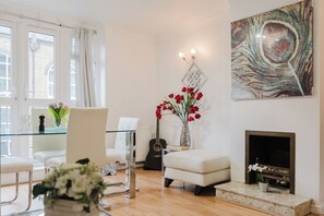 A modern living room with a fireplace, a glass coffee table, a white sofa, and a decorative wall piece. - Gated SE1 Mews House | Free Parking & Balcony (London)