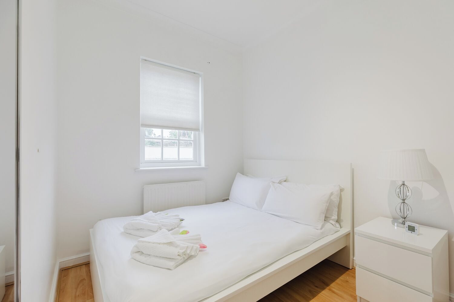 Ein schlicht eingerichtetes Schlafzimmer mit einem Einzelbett, einem Nachttisch mit Lampe und einem Fenster mit Jalousien.