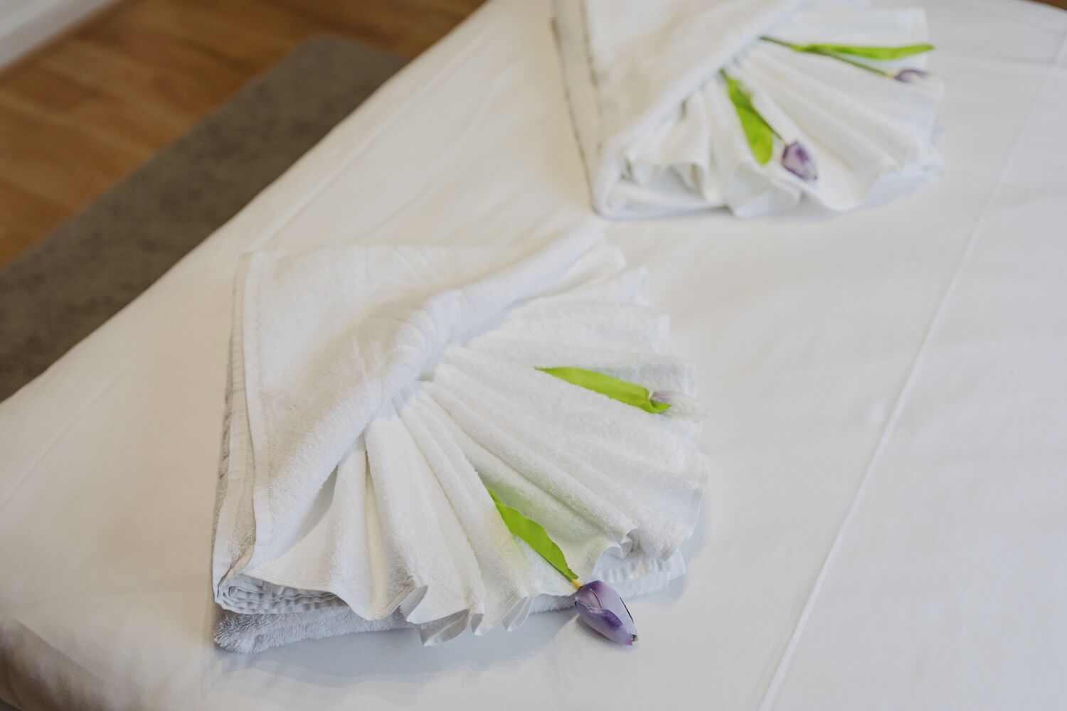Two neatly folded towels with green leaves on a bed.