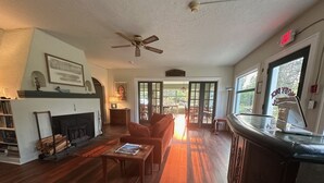 A spacious living room with a fireplace, a ceiling fan, and a view of the outdoors through large windows. - Moby Dick Hotel (Ocean Park)