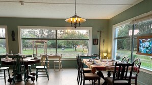A dining room with a large table set for six, surrounded by chairs, a chandelier, and large windows offering a view of the outdoors. - Moby Dick Hotel (Ocean Park)
