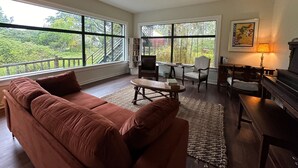 A spacious living room with a large window overlooking a lush garden, a cozy brown sofa, a wooden coffee table, and a piano. - Moby Dick Hotel (Ocean Park)