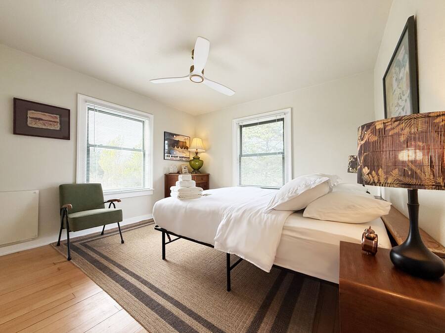 A bedroom with a bed, a chair, a lamp, and a ceiling fan.