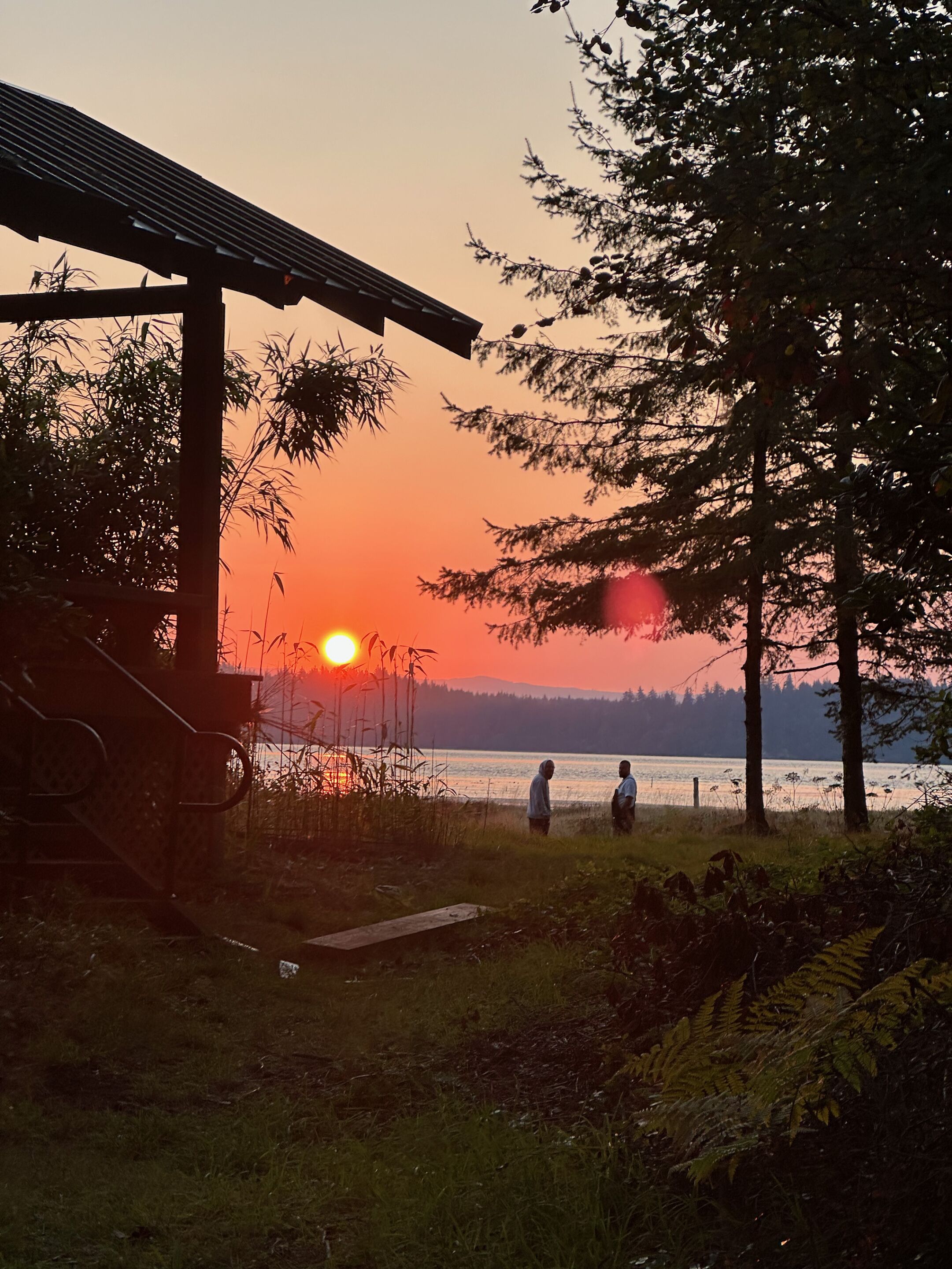 A sunset view with a wooden structure and a lake.
