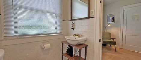 Et badeværelse med toilet, håndvask og et vindue med persienner.