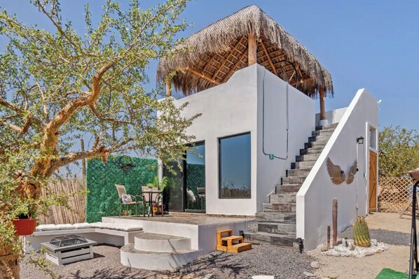 Ein modernes Haus mit Strohdach, einer Glastür und einer Treppe, die zu einer zweiten Etage führt.
