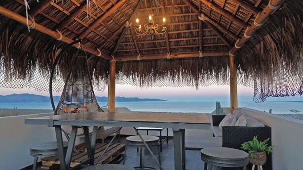 A beachside bar with a thatched roof, wooden tables, and chairs, overlooking the sea. - Rancho Baja Unknown (El Sargento)