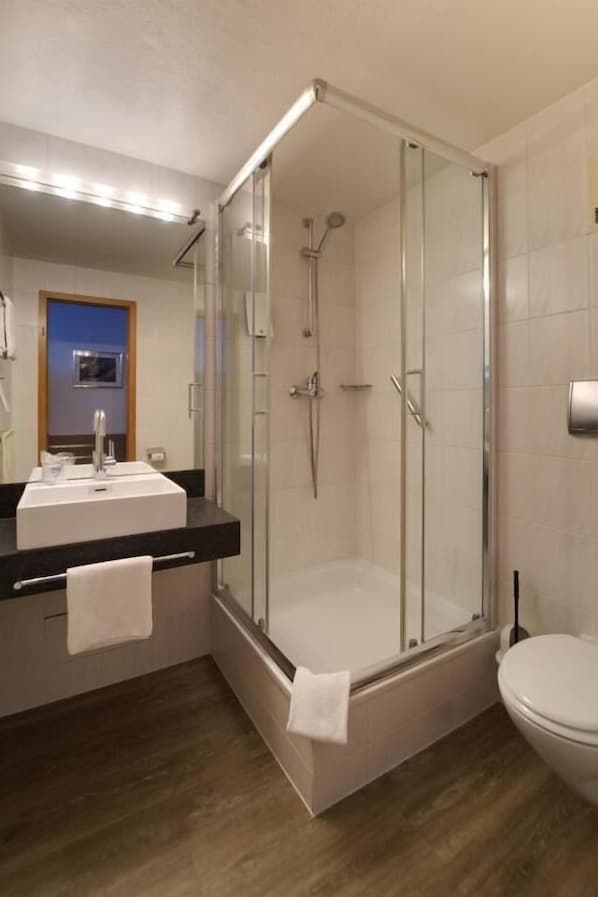 Ein modernes Badezimmer mit einer gläsernen Duschkabine, einem Waschbecken mit Spiegel und einer Toilette.