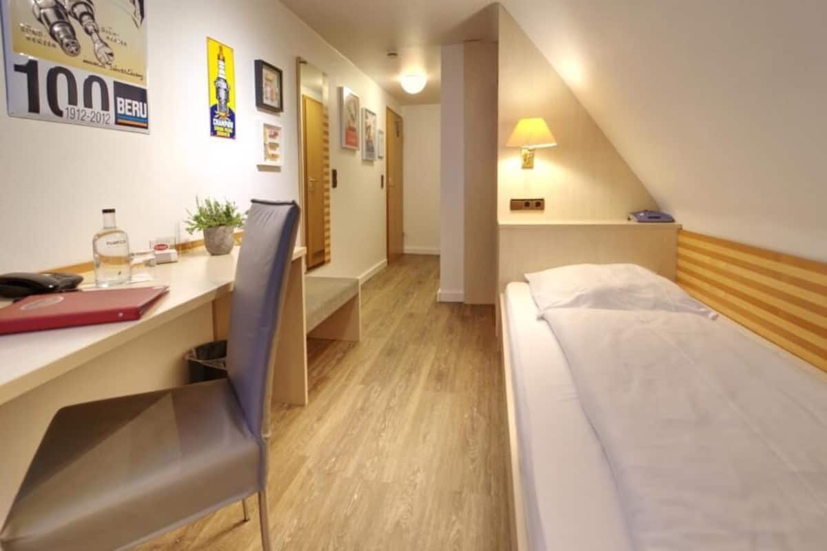 A hotel room with a bed, desk, chair, lamp, and a small plant.
