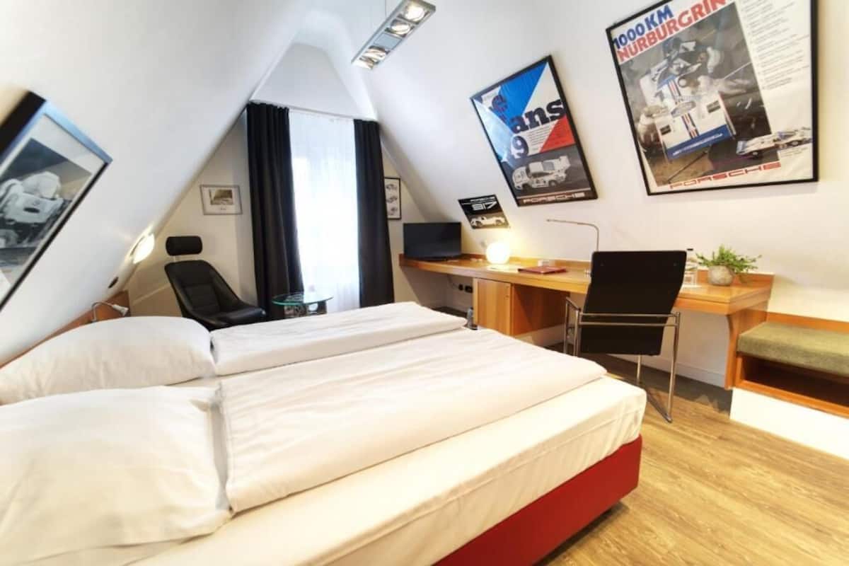 A hotel room with a bed, desk, chair, and a poster on the wall.