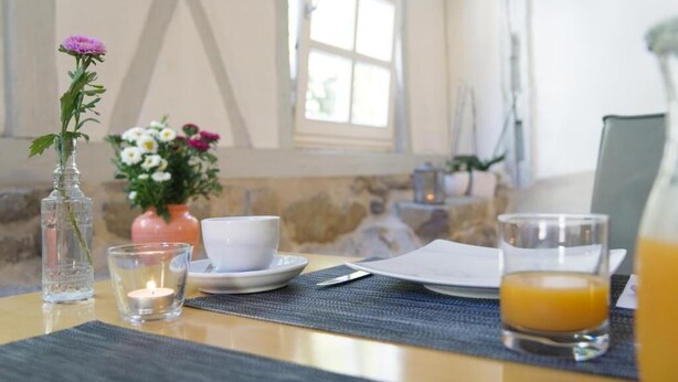 A breakfast setup with a vase of flowers, a candle, a cup, a glass of orange juice, and a plate of food on a table. - Reinhardts Garni Automobilia Hotel  (Bietigheim-Bissingen)