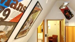 A hallway with a sloped ceiling, wooden benches, and a framed poster on the wall. - Reinhardts Garni Automobilia Hotel  (Bietigheim-Bissingen)