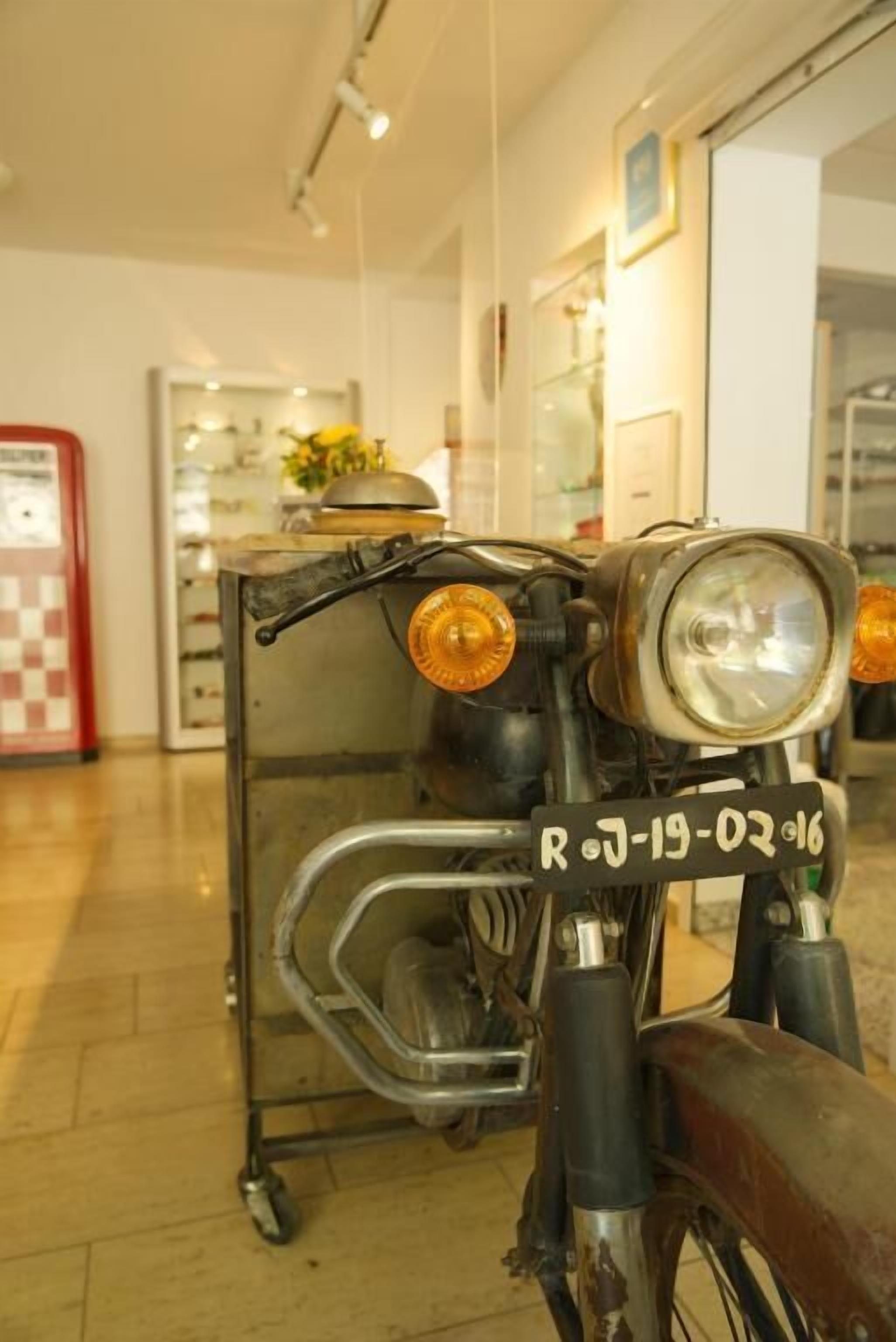 Une moto ancienne avec une plaque d’immatriculation, un chariot en métal et une cabine téléphonique rouge en arrière-plan.